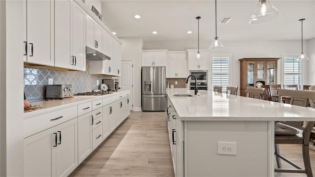 kitchen with white cabinetry, stainless steel appliances, sink, and a kitchen island with sink