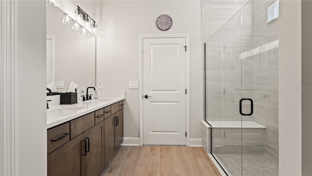 full bath featuring wood finished floors, double vanity, a stall shower, and a sink