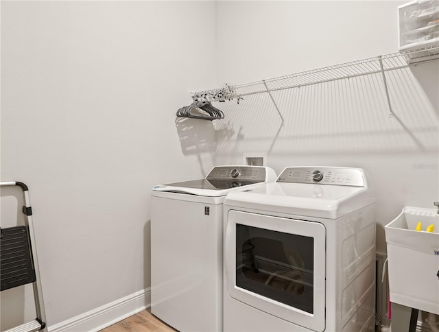clothes washing area featuring laundry area, light wood-style floors, washing machine and clothes dryer, a sink, and baseboards