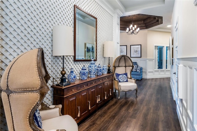 living area featuring dark wood-style flooring, a notable chandelier, a tray ceiling, a decorative wall, and wainscoting
