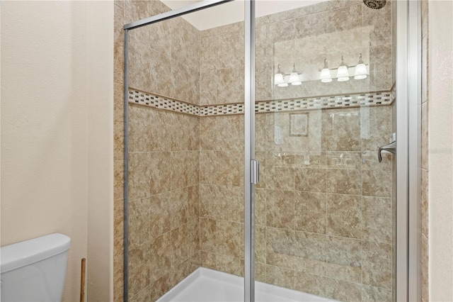 bathroom featuring a shower with door and toilet