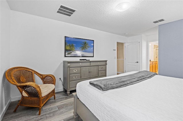 bedroom with connected bathroom, a textured ceiling, and light wood-type flooring