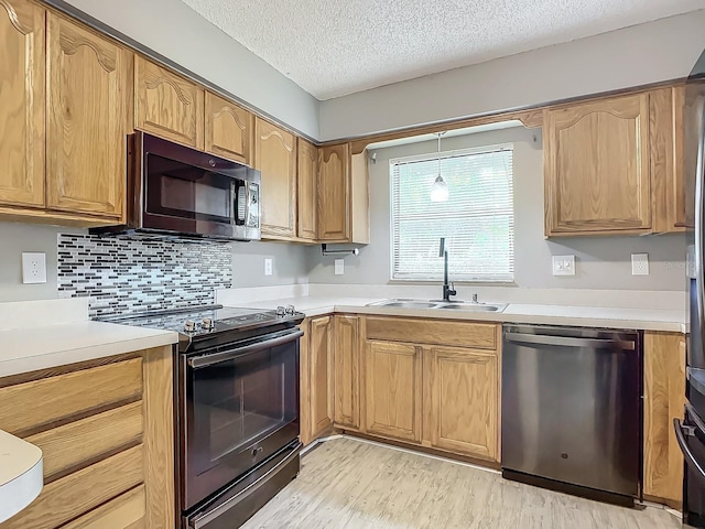 kitchen with range with electric stovetop, dishwasher, sink, light wood-type flooring, and a textured ceiling