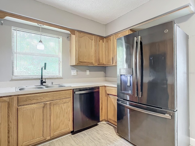 kitchen featuring appliances with stainless steel finishes, pendant lighting, sink, a textured ceiling, and light hardwood / wood-style flooring