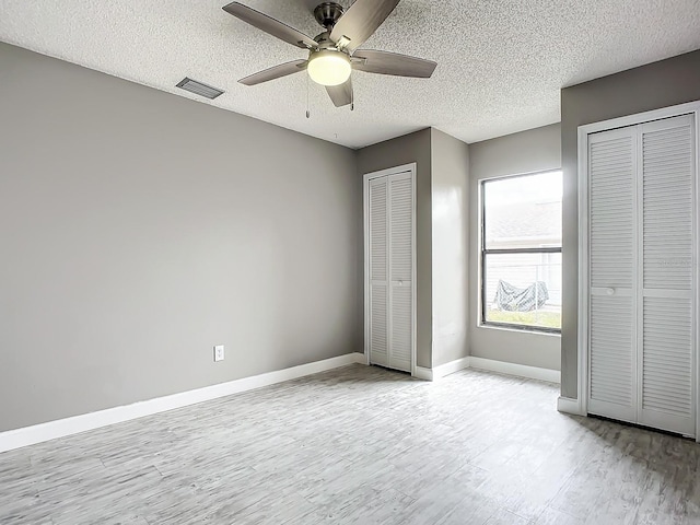 unfurnished bedroom featuring two closets, a textured ceiling, light hardwood / wood-style floors, and ceiling fan