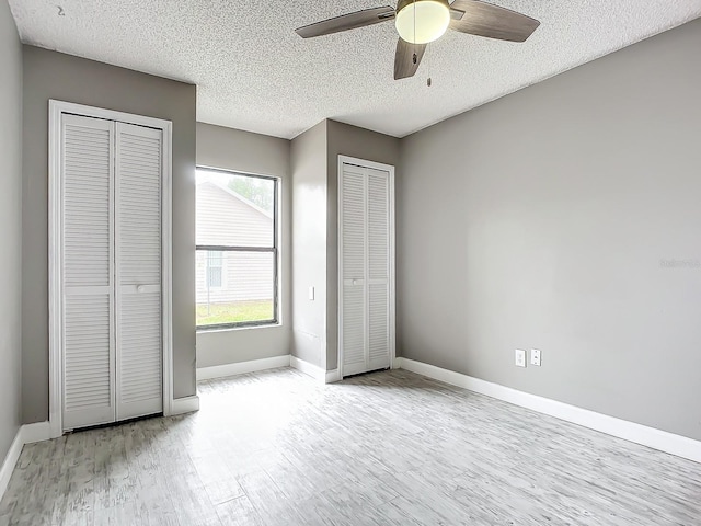 unfurnished bedroom featuring ceiling fan, a textured ceiling, multiple closets, and light wood-type flooring