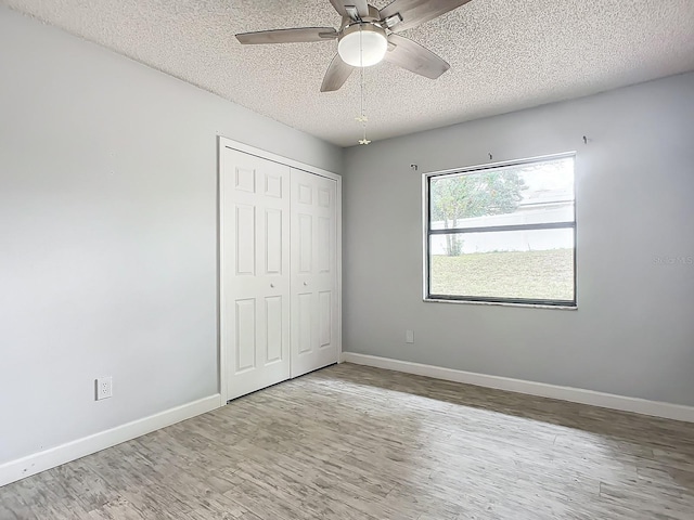 unfurnished bedroom with hardwood / wood-style flooring, ceiling fan, a closet, and a textured ceiling