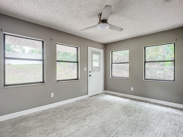 unfurnished room with a textured ceiling, a wealth of natural light, light hardwood / wood-style floors, and ceiling fan