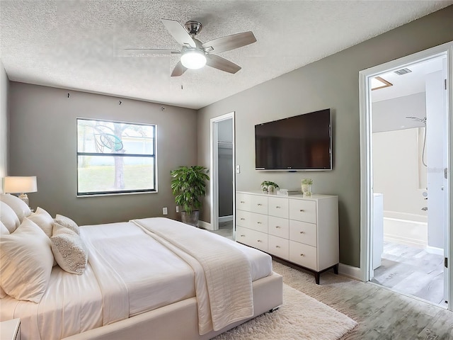 bedroom featuring ceiling fan, ensuite bathroom, light hardwood / wood-style floors, and a textured ceiling