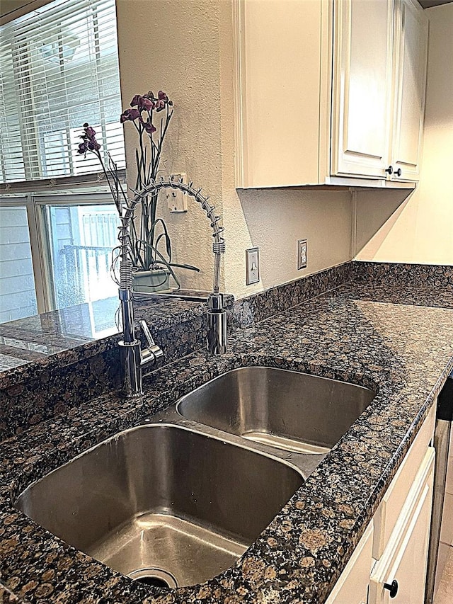 interior details featuring white cabinetry, dark stone counters, and sink