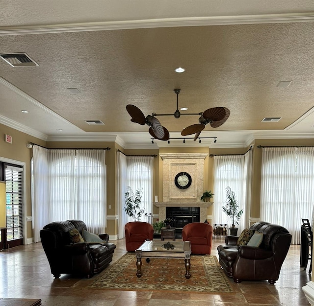 living room with ceiling fan, a textured ceiling, a tiled fireplace, and ornamental molding