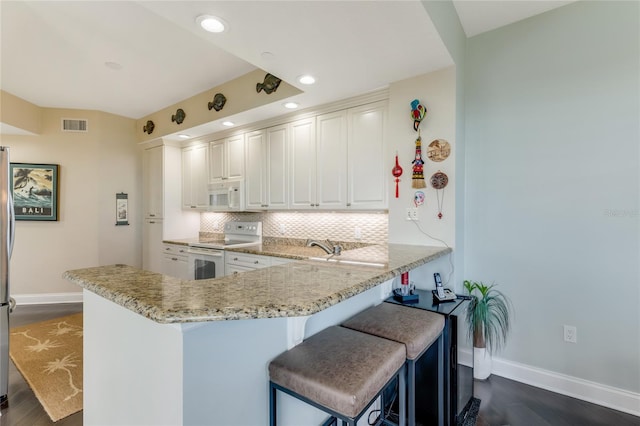 kitchen with white cabinetry, kitchen peninsula, dark hardwood / wood-style floors, a breakfast bar area, and white appliances