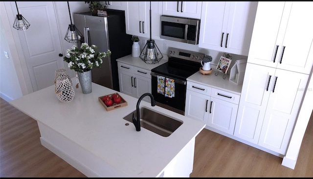 kitchen with white cabinets, hanging light fixtures, sink, light hardwood / wood-style flooring, and appliances with stainless steel finishes