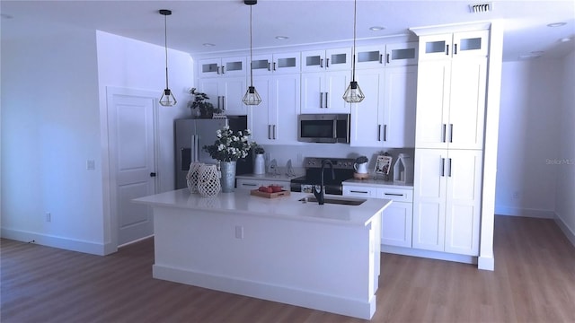 kitchen with appliances with stainless steel finishes, a center island with sink, white cabinetry, and pendant lighting