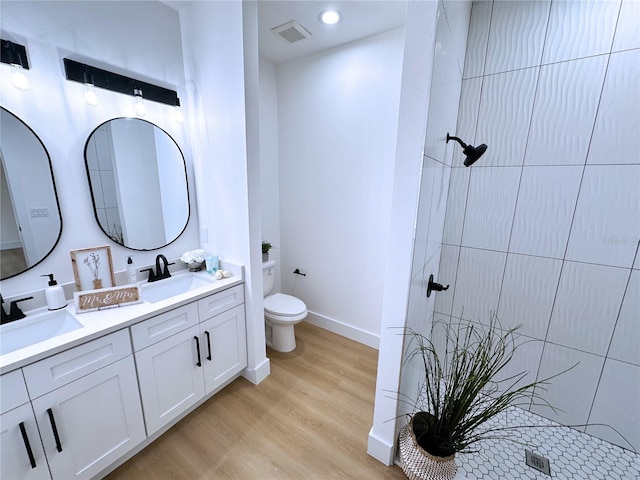 bathroom with wood-type flooring, vanity, a tile shower, and toilet