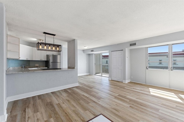 unfurnished living room featuring a textured ceiling, visible vents, light wood finished floors, and baseboards