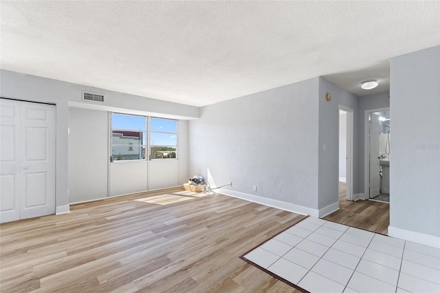 interior space with a textured ceiling, visible vents, wood finished floors, and baseboards