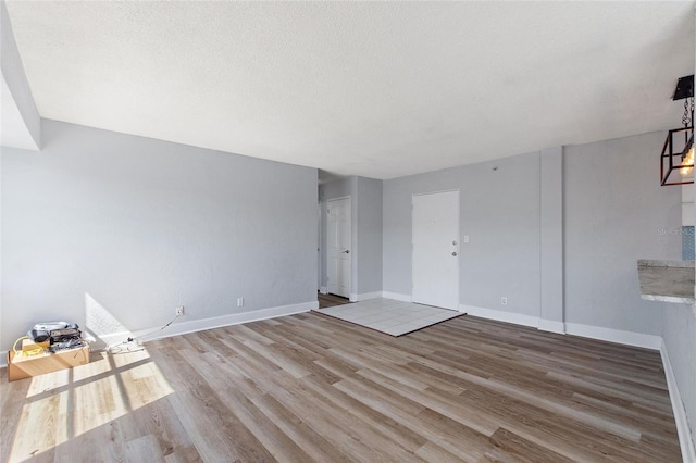 unfurnished living room with a textured ceiling, wood finished floors, and baseboards