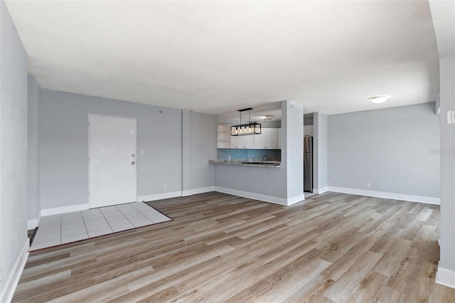 unfurnished living room with an inviting chandelier, baseboards, and light wood-type flooring