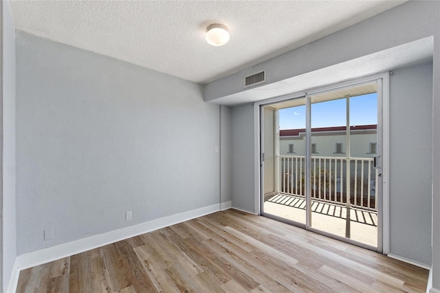 spare room with baseboards, visible vents, wood finished floors, and a textured ceiling