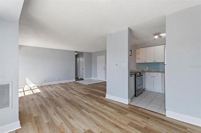 unfurnished living room featuring baseboards, light wood-type flooring, visible vents, and a textured ceiling