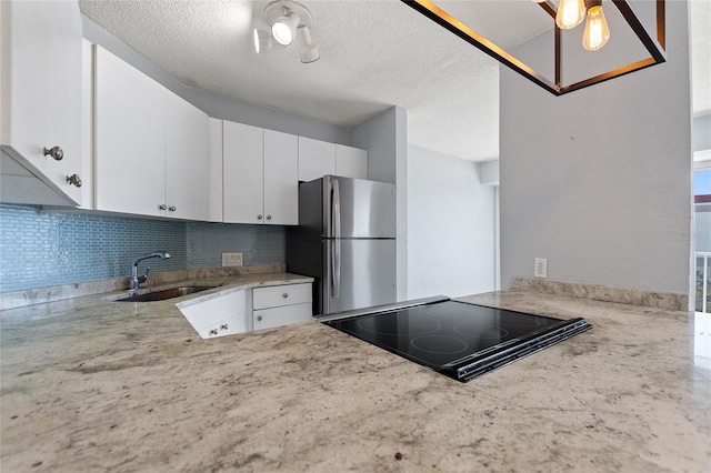 kitchen featuring tasteful backsplash, light stone countertops, freestanding refrigerator, stovetop with downdraft, and a sink
