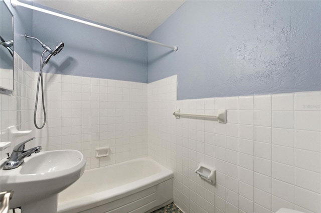 bathroom featuring washtub / shower combination, tile walls, and sink