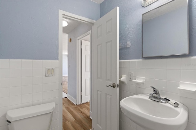 half bath featuring wood finished floors, tile walls, a wainscoted wall, toilet, and a sink