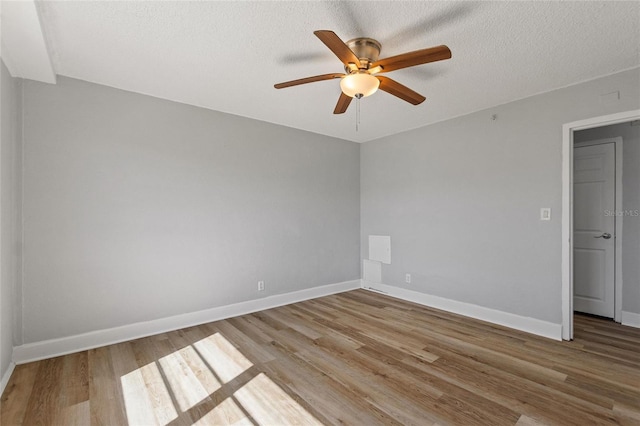 empty room with a textured ceiling, wood finished floors, a ceiling fan, and baseboards