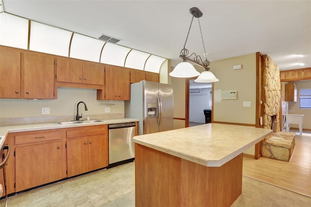 kitchen with appliances with stainless steel finishes, sink, light wood-type flooring, a kitchen island, and pendant lighting