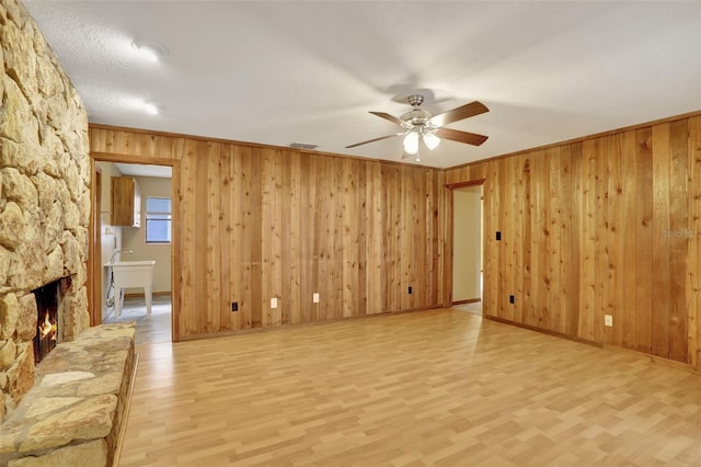 unfurnished living room featuring ceiling fan, light hardwood / wood-style flooring, a fireplace, crown molding, and wooden walls