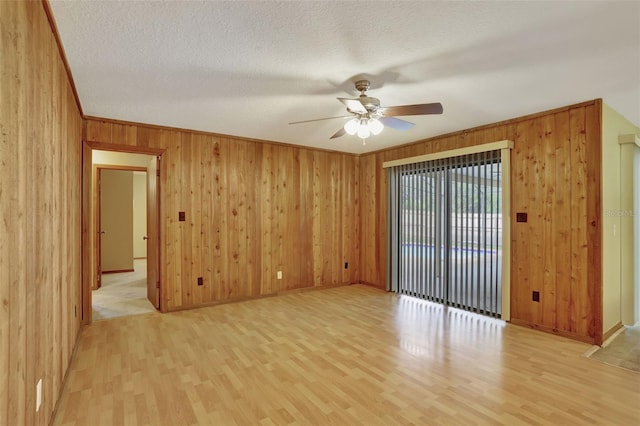 empty room with wood walls, light hardwood / wood-style flooring, a textured ceiling, and ceiling fan