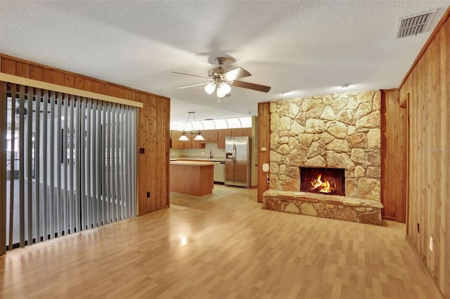 unfurnished living room with a textured ceiling, wooden walls, light wood-type flooring, and ceiling fan