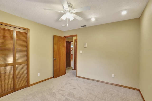 unfurnished bedroom featuring a closet, ceiling fan, a textured ceiling, and light colored carpet