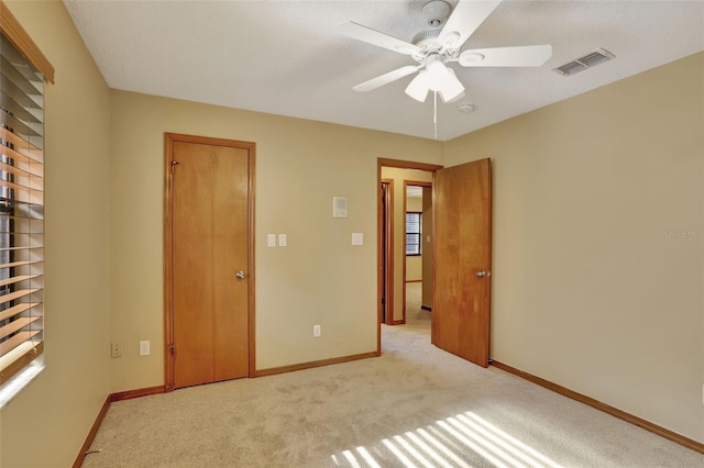 unfurnished bedroom with ceiling fan, multiple windows, and light colored carpet