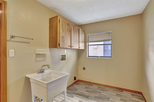 laundry room featuring sink, a textured ceiling, cabinets, washer hookup, and light hardwood / wood-style flooring