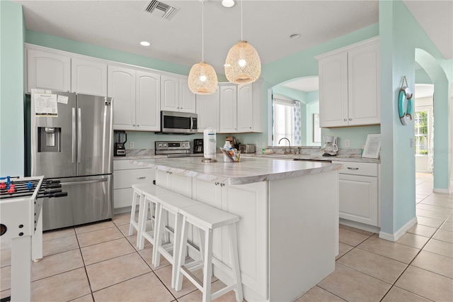 1055 Lake Berkley Dr, Kissimmee, FL 34746 - kitchen featuring appliances with stainless steel finishes, arched walkways, a center island, white cabinets, and light tile patterned floors