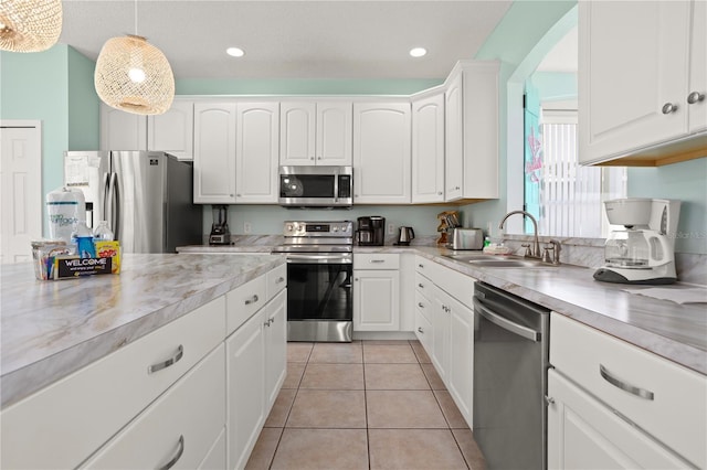 kitchen with sink, decorative light fixtures, light tile patterned flooring, white cabinetry, and stainless steel appliances