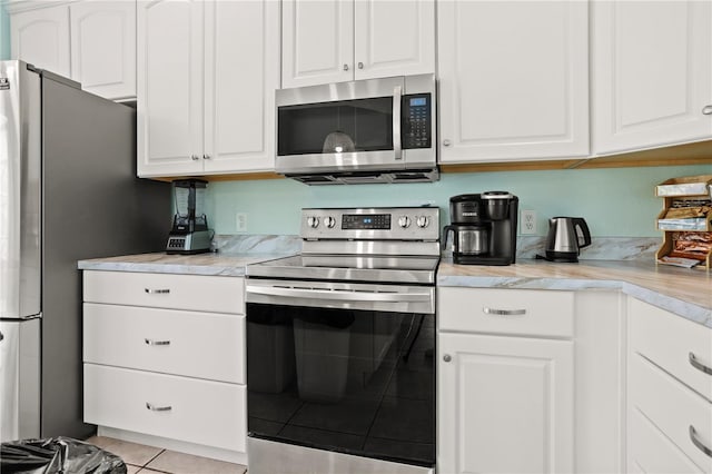 kitchen featuring appliances with stainless steel finishes, light tile patterned floors, and white cabinetry