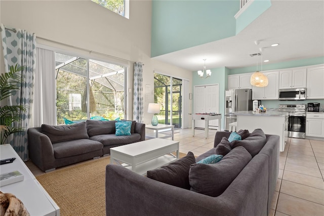 living room with a notable chandelier, a healthy amount of sunlight, light tile patterned flooring, and a high ceiling