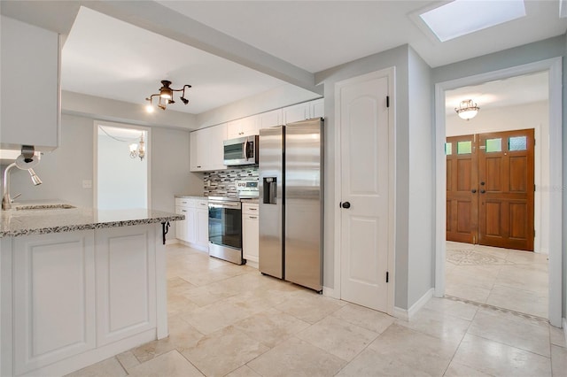 kitchen featuring decorative backsplash, white cabinets, appliances with stainless steel finishes, light stone countertops, and sink