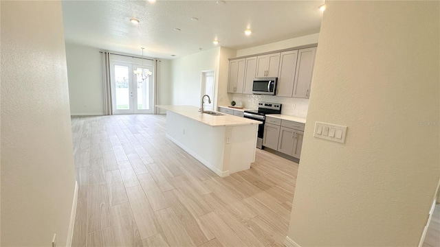 kitchen with gray cabinetry, sink, light hardwood / wood-style floors, stainless steel appliances, and a kitchen island with sink