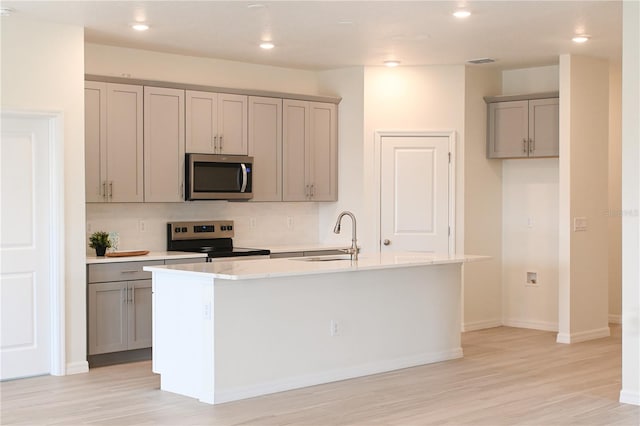 kitchen featuring a kitchen island with sink, light hardwood / wood-style flooring, gray cabinetry, sink, and appliances with stainless steel finishes