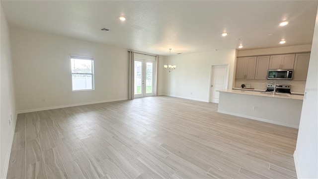 unfurnished living room with an inviting chandelier, light hardwood / wood-style flooring, and french doors