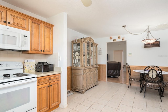 kitchen featuring light tile patterned floors, pendant lighting, white appliances, and wood walls