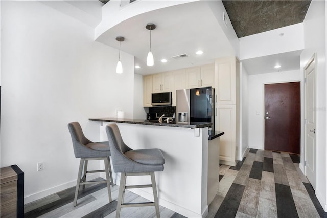 kitchen featuring light hardwood / wood-style flooring, kitchen peninsula, pendant lighting, appliances with stainless steel finishes, and tasteful backsplash