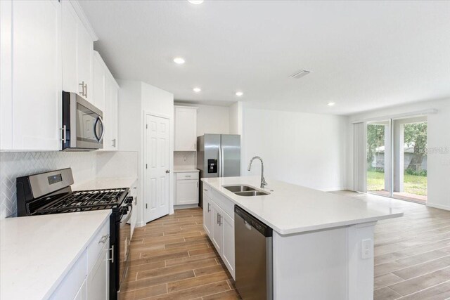 kitchen with sink, white cabinets, stainless steel appliances, and a center island with sink