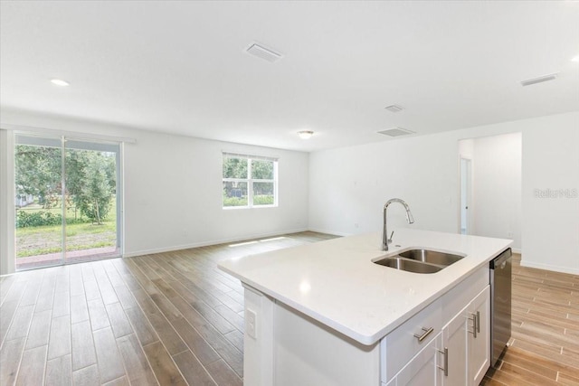 kitchen with stainless steel dishwasher, sink, white cabinetry, plenty of natural light, and an island with sink