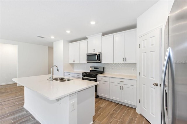 kitchen with sink, backsplash, a center island with sink, white cabinets, and appliances with stainless steel finishes