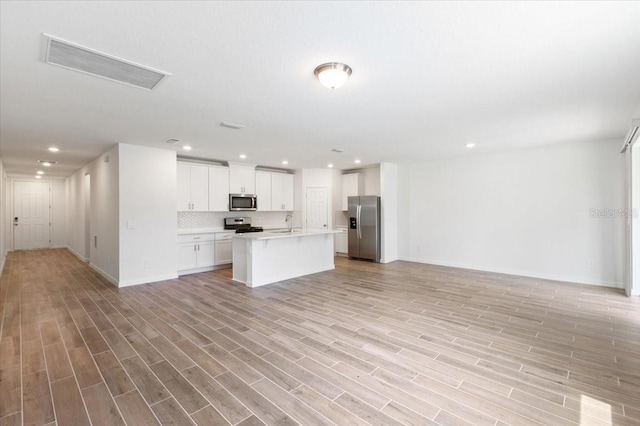 kitchen with white cabinets, light hardwood / wood-style flooring, an island with sink, appliances with stainless steel finishes, and tasteful backsplash